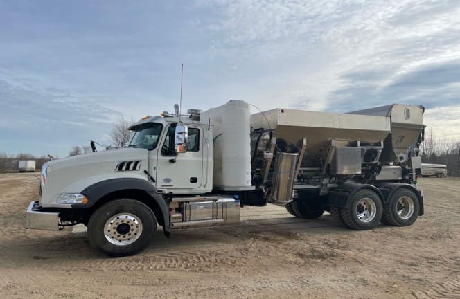 A white dump truck parked on top of a dirt field.