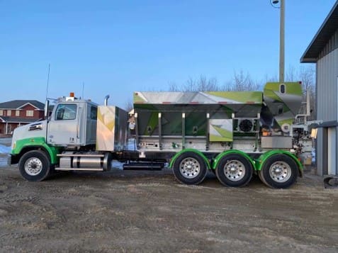 A large green truck parked in the dirt.